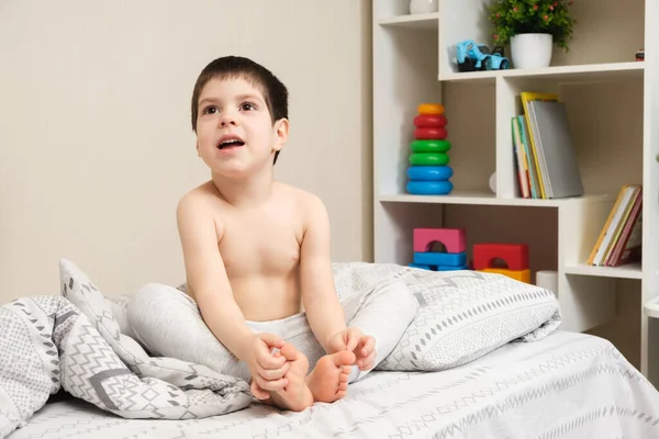 Retrato de un niño desnudo de 4 años mirando hacia los lados en una habitación de niños con un telón de fondo de juguetes —  Fotos de Stock
