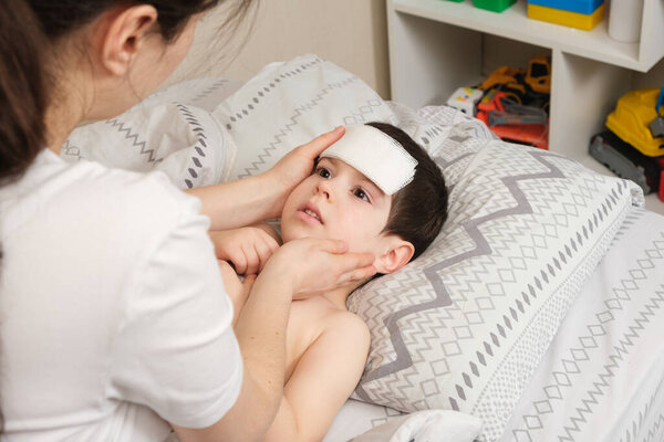 The mother cares for the feverish 4-year-old son, the child has a cooling compress on the forehead