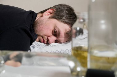 Sarhoş, alkolik bir adam, masada boş şişelerle yatakta yatıyor. Alkolizm ve alkol bağımlılığı sosyal bir sorundur