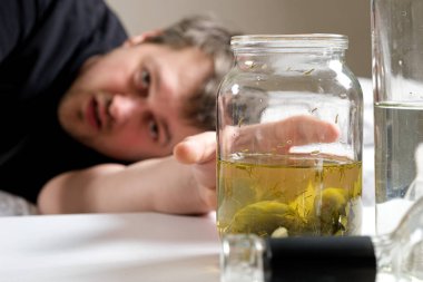 Alkol bağımlısı bir adam yatağa uzanır ve elini bir kavanoz salatalık salamurasına uzatır. Akşamdan kalmalık için halk ilaçları.