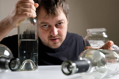 Alkolik bir adam masaya oturur, elinde bir şişe votkayla kameraya bakar. Alkol bağımlılığı, alkolizm ve hezeyan