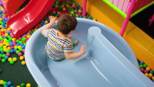 明るい未就学児の男の子が青いスライドからプールに降り 遊び場にボールがあります — ストック動画