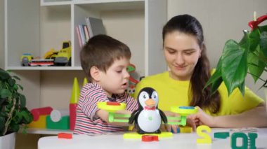 Anne ve oğul saymayı öğrenirler. Farklı renkte ağırlıklar, penguen şeklinde oyuncak pullarıyla ölçülür.