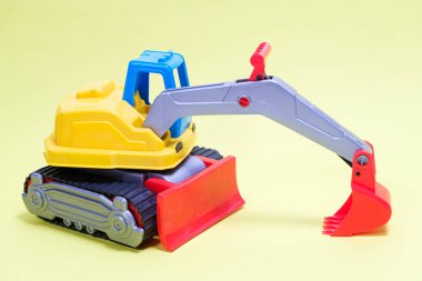 Sarı arka planda plastik kazıcı vagonu. Oyuncakçı ve çocuklar için kazı yapan inşaat makineleri.