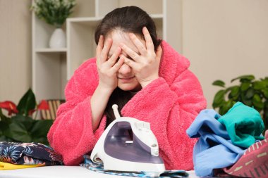 Yorgun kadın ütü masasında ütüyle giysileri ütüler ve ağlar. Ev kadınlarından bıkkınlık, günlük anneliğin can sıkıcı rutini.