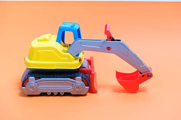 オレンジの背景に黄色の掘削機プラスチック車。おもちゃ屋や子供のための掘削のための建設機械車. — ストック写真
