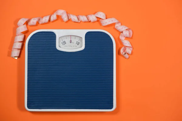 Floor blue scales and centimeter measuring tape on an orange background, top view. The concept of weight loss and weight control