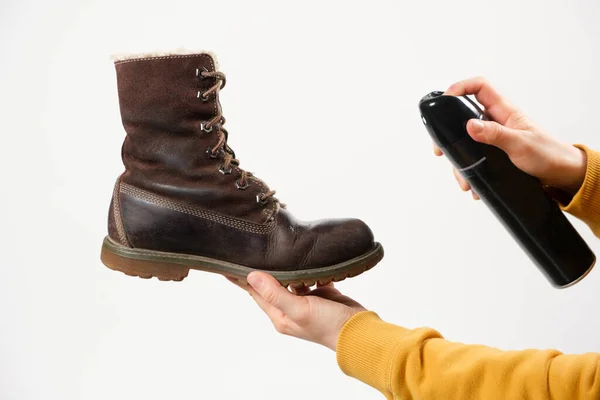 Uma mulher aplica o spray para botas de inverno de mulheres nubuck marrom. Cuidado repelente de água para sapatos, renovação e preservação da cor — Fotografia de Stock