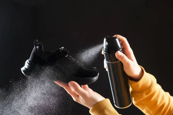 A woman applies a spray from a cylinder with a water-repellent liquid to childrens crumbs. Care for shoes, elimination of unpleasant odor.