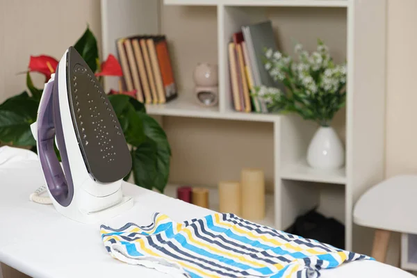 Strijkijzer op de strijkplank en kinder gestreept T-shirt. Verzorging van kleding, keramische zoolplaat. — Stockfoto