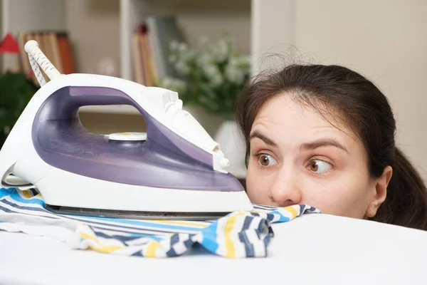 Een verbaasde vrouw kijkt naar het strijkijzer op de strijkplank. Tips voor het verzorgen van kleding — Stockfoto