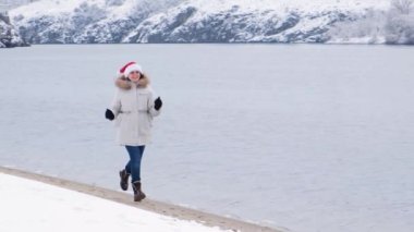 Güzel bir kadın kışın nehir boyunca koşar Noel Baba 'nın Noel şapkası kafasında.
