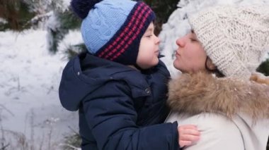 Anne ve oğul doğada öpüşürler, karla kaplı kış ormanı.