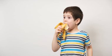 4 yaşında bir çocuk bir muz yer. Beyaz arkaplandaki yazı için uzun afiş. Anaokulu çocukları için meyve ve vitaminler