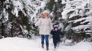Anne ve oğlu karlı bir kış ormanında koşuyorlar, mutlu ebeveynlik ve aile tatili, yavaş çekim.