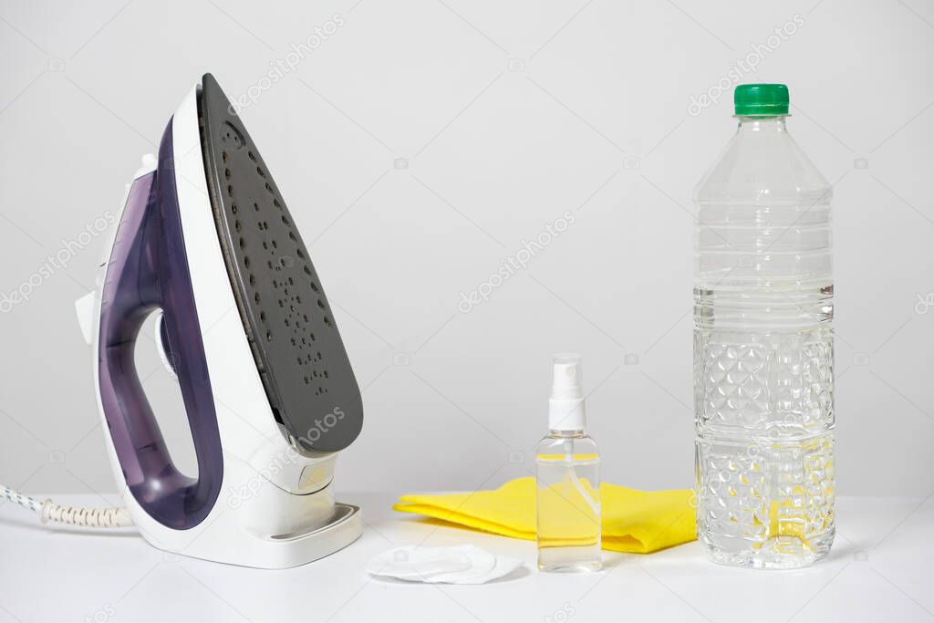 Iron and means for cleaning the sole of the iron - a special liquid and a bottle of vinegar on a white background. Ways to clean the iron.