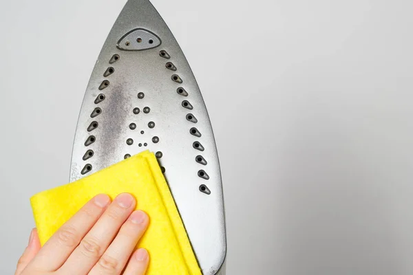 Die Hausfrau wischt die schmutzige Oberfläche des Bügeleisens mit einem gelben Lappen ab. Reinigung des Eisens von Kohlenstoffablagerungen — Stockfoto