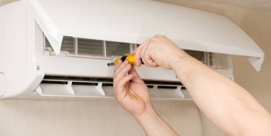 Usta, klima kapağını tornavidayla söküyor. Klimaların profesyonel bakım ve onarımı