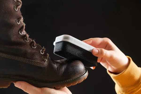 The woman cleanses and applies the cream to brown nubuck womens winter boots with a sponge. On a black background, close-up — Stock Photo, Image