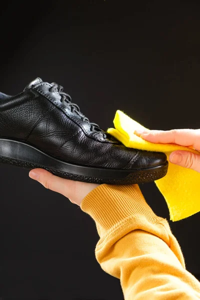 A man wipes leather mens black shoes with a yellow shoe rag. Cleaning from dust, shoe care