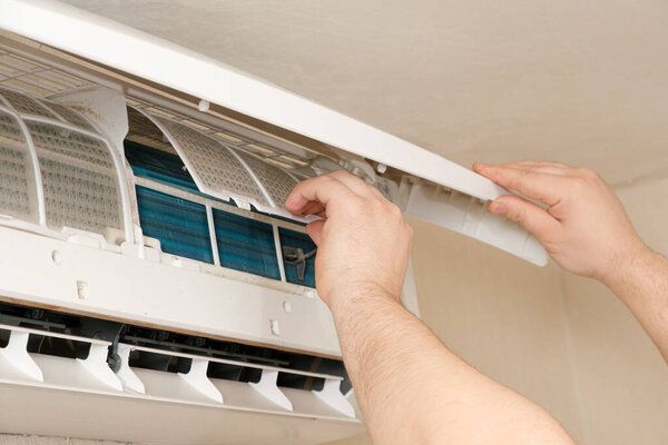 The master removes the dusty filter of the air conditioner. Maintenance and repair of air conditioners.