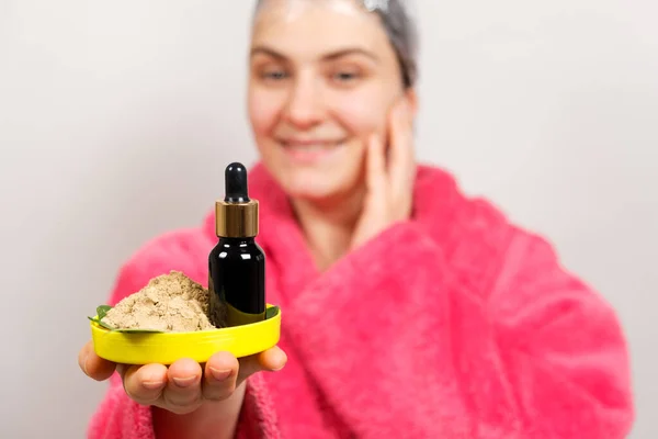 Una mujer guarda cosméticos naturales para el cuidado del cabello - una botella de aceites y ubtan, un exfoliante de hierbas —  Fotos de Stock