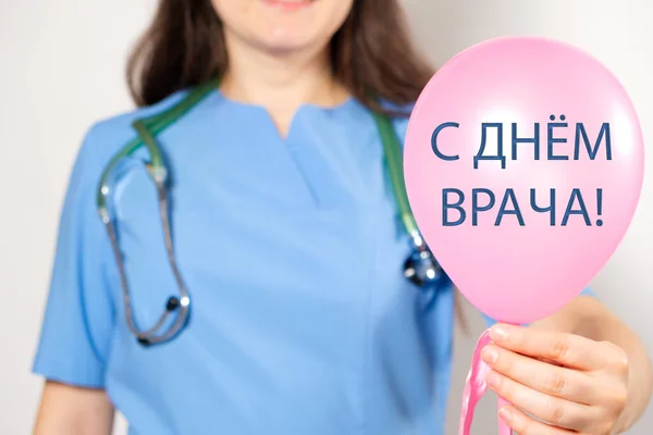 Lékař v modré uniformě drží modrý balón s textem na ruštině, přeložen z ruštiny: Šťastný den doktorů — Stock fotografie