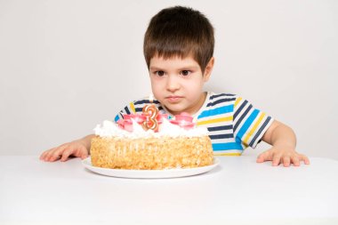 Çizgili tişörtlü bir çocuk elinde mum şeklinde büyük bir pasta tutuyor.