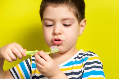 4 yaşında yakışıklı bir çocuk sarı bir arka planda diş fırçası tutuyor, metin için kopyalama alanı