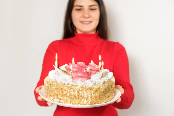 Una morena vestida de rojo sostiene un gran pastel blanco con velas, pide un deseo —  Fotos de Stock