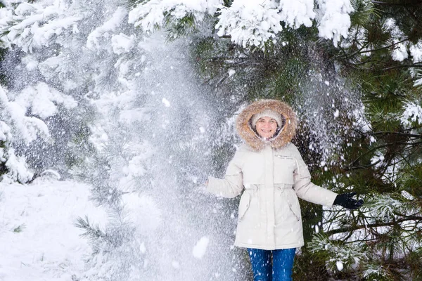 Una donna in una foresta innevata invernale sorride guardando la macchina fotografica, i fiocchi di neve volano. — Foto Stock