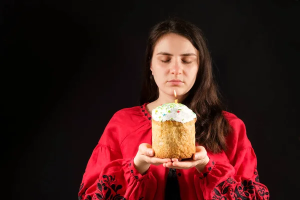 Молода жінка з закритими очима тримає пиріг з запаленою свічкою на чорному тлі, місце для тексту — стокове фото