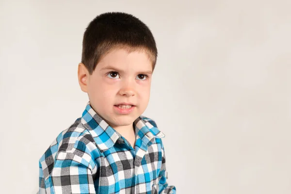 Um menino pré-escolar de 4 anos olha beligerantemente, franzindo as sobrancelhas em um fundo branco com espaço para texto. Emoções das crianças. — Fotografia de Stock