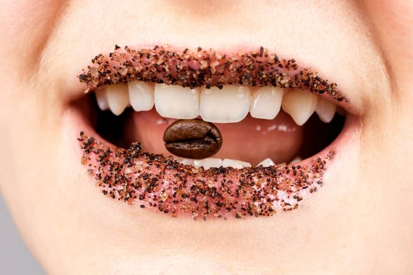 Ein Kaffee-Peeling auf den Lippen einer Frau und eine Kaffeebohne im Mund. Lippenpflege, Peeling zu Hause — Stockfoto