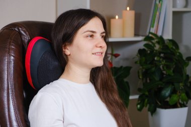 Bir kadın masaj yastığıyla bir sandalyeye oturur ve boyun masajı yapar..