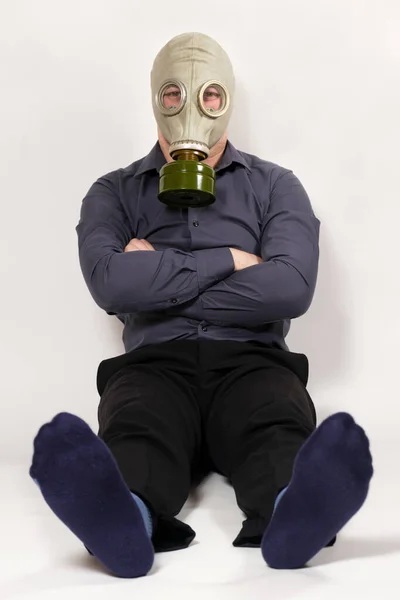 Gaz maskeli bir adam beyaz arka planda oturur, bacakları kokar. Erkeklerde hoş olmayan çorap kokusu. — Stok fotoğraf