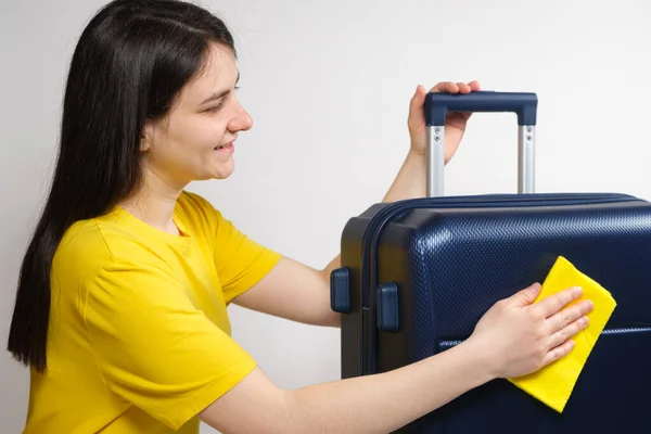 Жінка протирає подорожню пластикову блакитну валізу жовтою ганчіркою. Догляд за валізою, видалення подряпин і пилу . — стокове фото