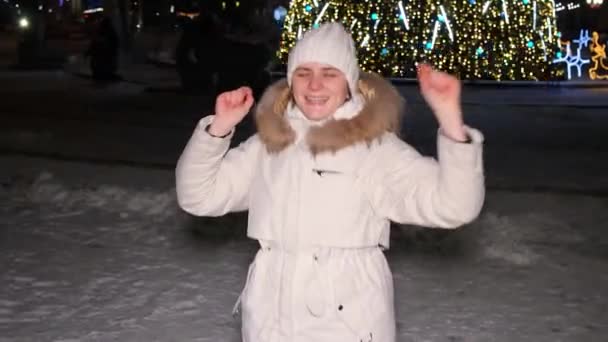 Молодая женщина прыгает и веселится возле елки на открытом воздухе, идет снег. — стоковое видео