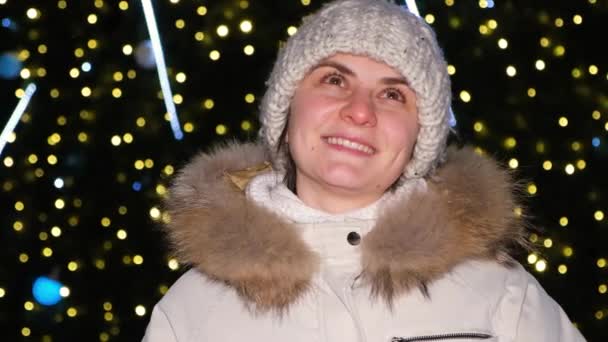 하얀 모자와 재킷을 입은 한 여성 이 크리스마스 트리 근처에 서서 눈을 감고 웃는 꿈을 꾼다. — 비디오