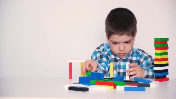 Um menino de 4 anos brinca com blocos de madeira multicoloridos, constrói torres sobre um fundo branco. Brinquedos naturais para o desenvolvimento de habilidades lógicas e motoras em crianças. — Vídeo de Stock