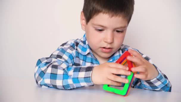 A boy of 4 years plays with a magnetic constructor, gets angry, knocks his hands and details on the table, throws toys — Vídeo de Stock