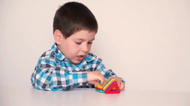 A preschool boy cheerfully plays with a magnetic constructor, laughs and speaks on a white background