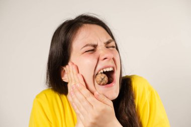 A woman gnaws on a walnut, opening her mouth wide, breaking a tooth or dislocating the temporomandibular joint, her jaw has moved away.