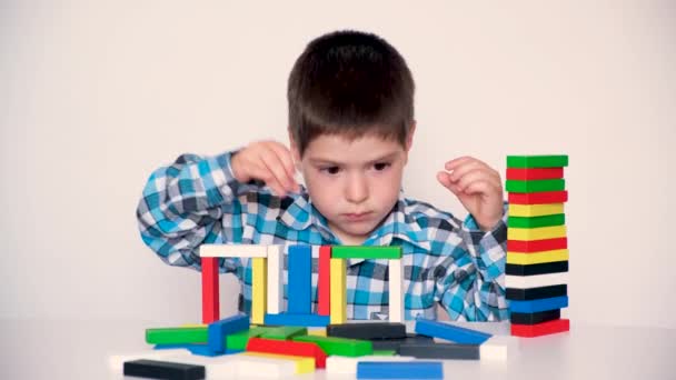 Un niño de 4 años juega con bloques de madera multicolores, construye torres sobre un fondo blanco. Juguetes naturales para el desarrollo de la lógica y las habilidades motoras en los niños. — Vídeo de stock