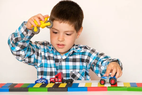 Menino pré-escolar 4 anos brinca com carros e brinquedos, jogos para crianças, loja de brinquedos em um fundo branco. — Fotografia de Stock