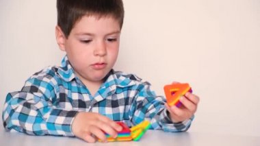 A preschool boy cheerfully plays with a magnetic constructor, laughs and speaks on a white background