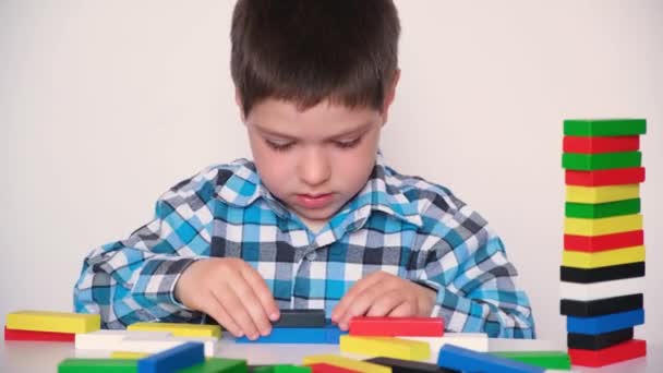 Ένα παιδί προσχολικής ηλικίας παίζει με πολύχρωμα ξύλινα μπλοκ για ένα εργοτάξιο, καταστρέφει έναν πύργο και μιλάει. — Αρχείο Βίντεο