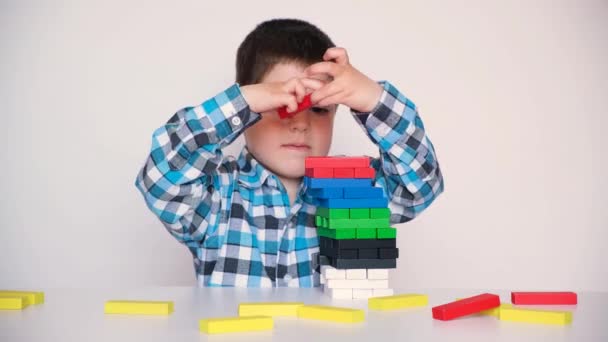 Un niño preescolar juega, construye cuidadosamente una torre de bloques de madera de colores — Vídeo de stock