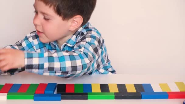 Un garçon d'âge préscolaire joue activement les voitures, détruit la route des blocs multicolores, crie et frappe la table avec des jouets — Video