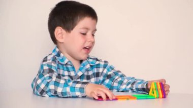 A preschool boy cheerfully plays with a magnetic constructor, laughs and speaks on a white background